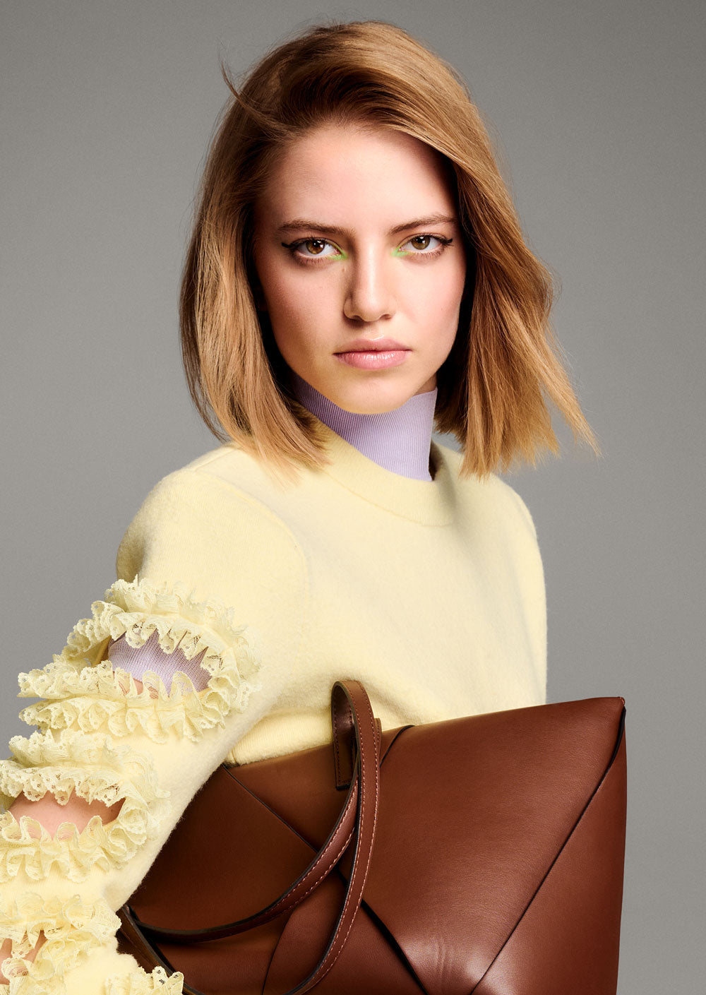 TONI & GUY EDITION ONE YENTE CHIC CROP Woman holding a brown leather handbag against a gray background