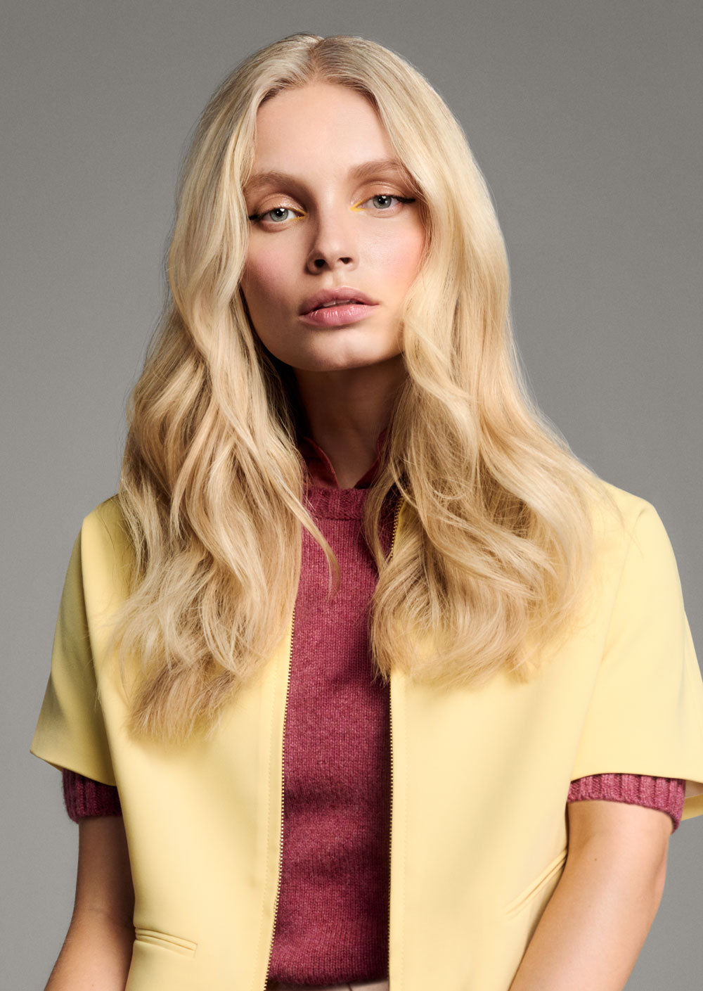 TONI & GUY EDITION ONE MARIA SUPERMODEL CUT - Woman with long blonde hair wearing a yellow cardigan over a red sweater on a gray background