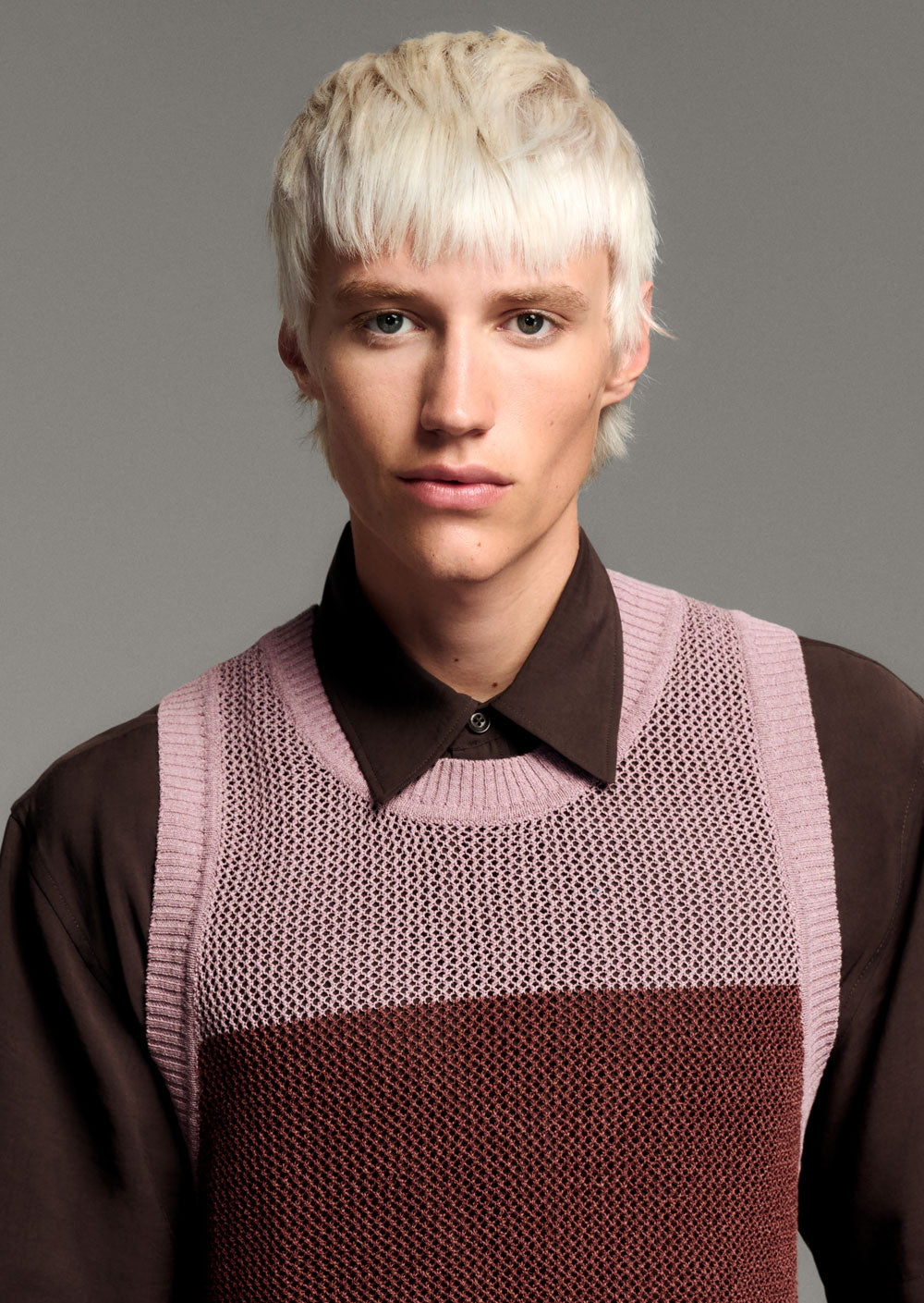 TONI & GUY EDITION ONE EDEN MOD CUT Person wearing a brown shirt with a pink knitted vest against a gray background